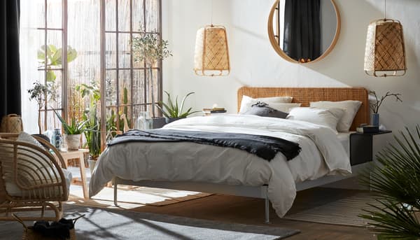 A bright bedroom with lots of natural materials, like rattan and bamboo. Big glass doors and an outdoor area next to the bed.
