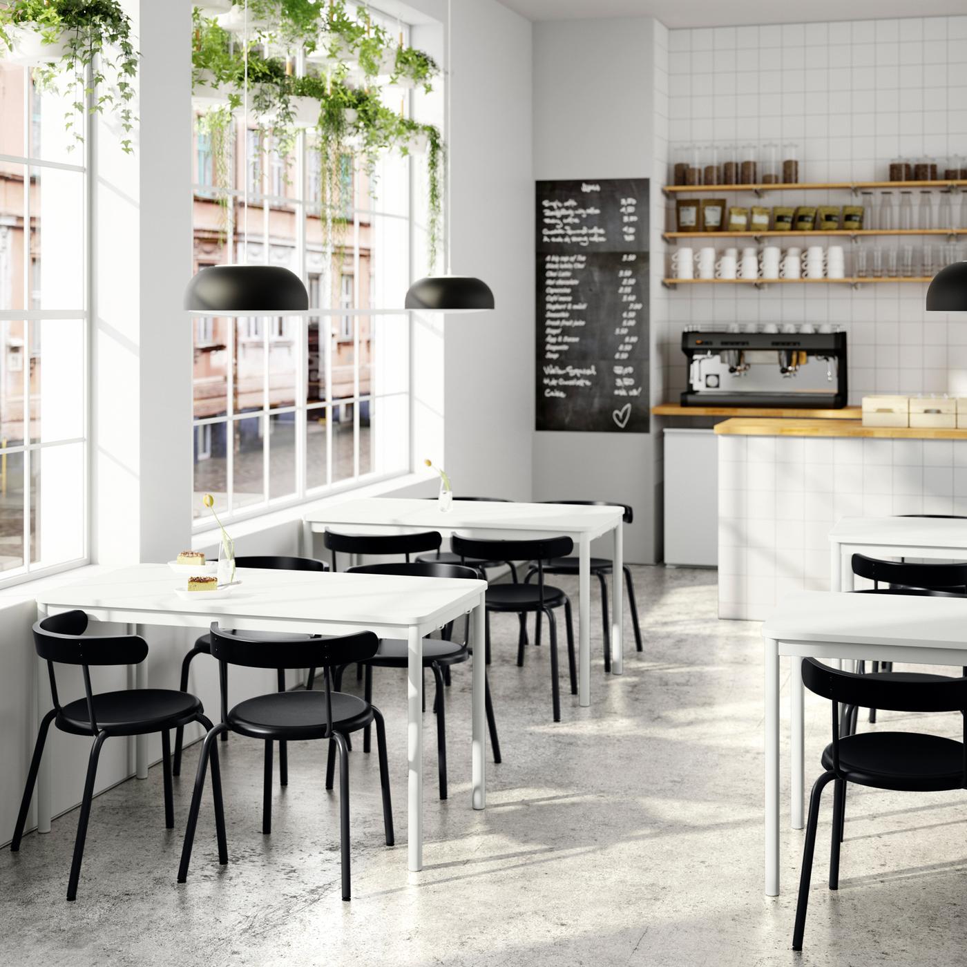 A bright cafe with TOMMARYD tables, anthracite chairs, a counter area with a coffee machine and a black and white menu board.