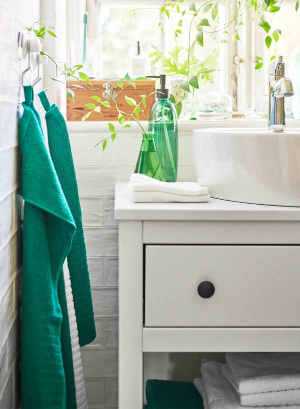 A bright green bottle and vase sit atop a white wash stand, while two green towels hang to its left.