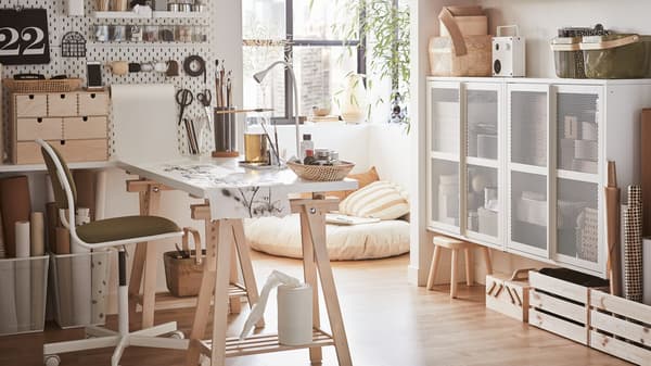 A bright home office with a white desk, a white/yellow green swivel chair and a white pegboard with crafting materials.