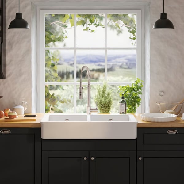 A bright kitchen sink area with dark cabinets, a large window and potted herbs on the sill.