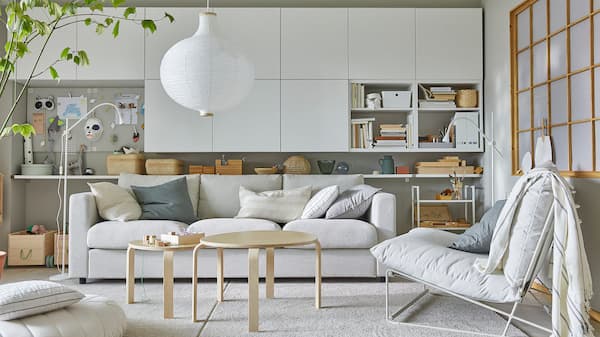 A bright living room with a HAVSTA easy chair, many white wall-mounted cabinets and a round, white pendant lamp.