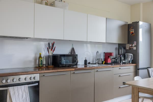 A bright, modern kitchen with white cabinets, a countertop, appliances, and kitchen utensils.