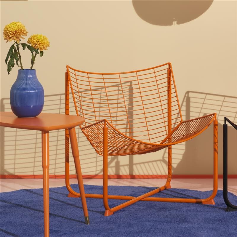 A bright orange steel armchair and matching coffee table sit on a blue rug, with a blue vase of flowers on the table.