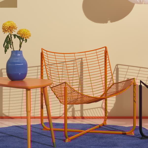 A bright orange steel armchair and matching coffee table sit on a blue rug, with a blue vase of flowers on the table.	
