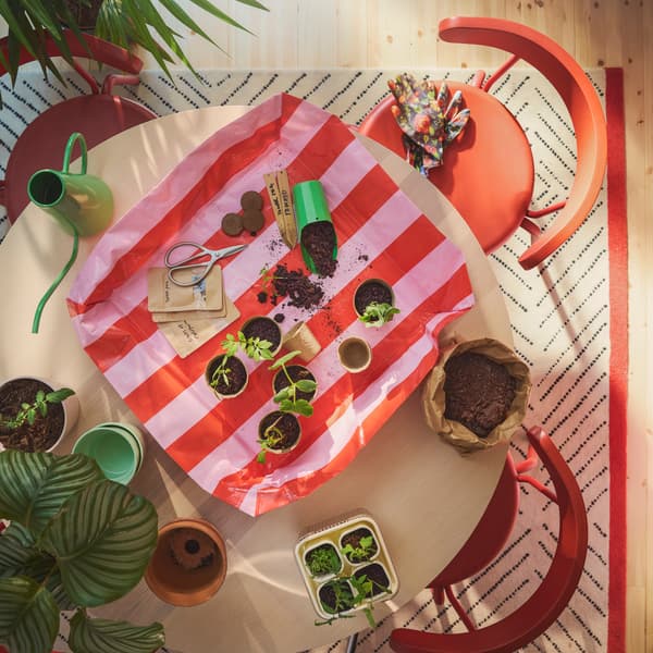 A bright pink and red striped DOFTRIPS potting mat placed on a round table filled with small pots, seedlings and tools.