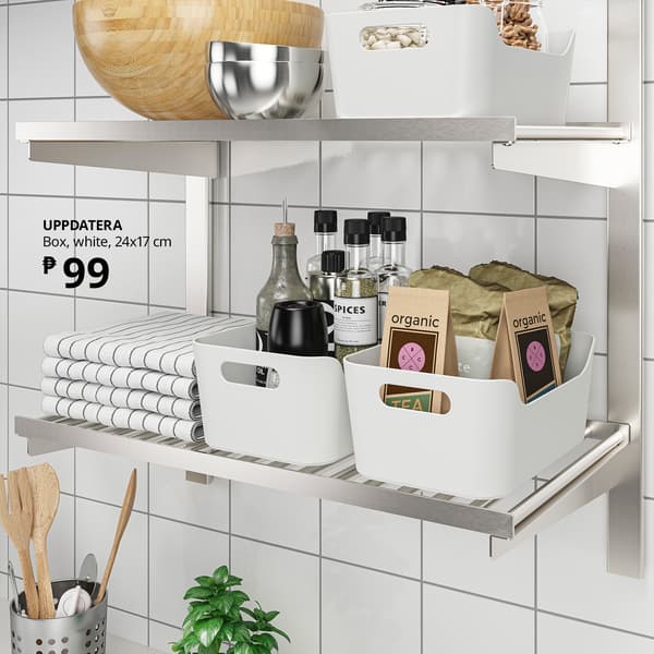 A bright tiled kitchen shows white Uppdatera storage boxes holding spices, tea and organic packets beside folded towels; a label advertises the box for ₱99.