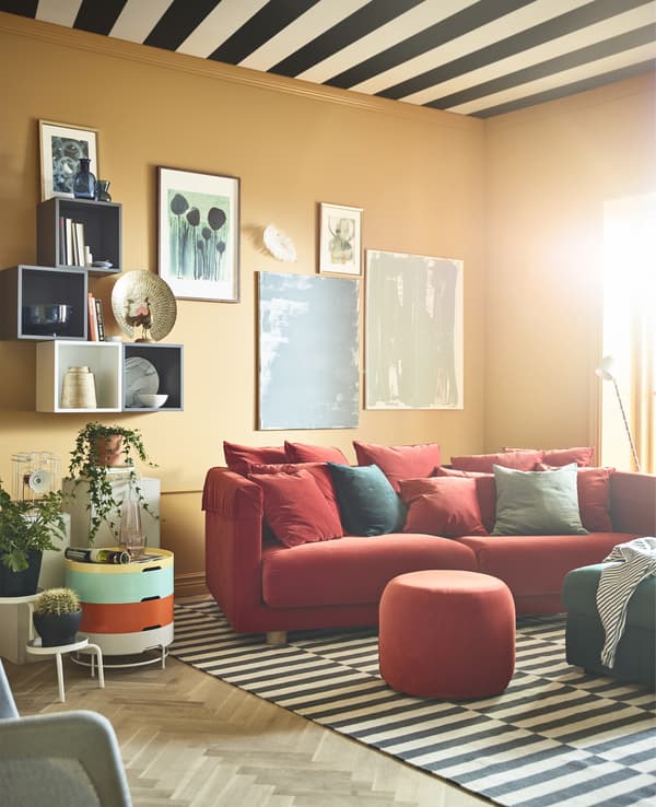 A brightly colored living room with ochre walls is burnished with a red sofa and ottomans.