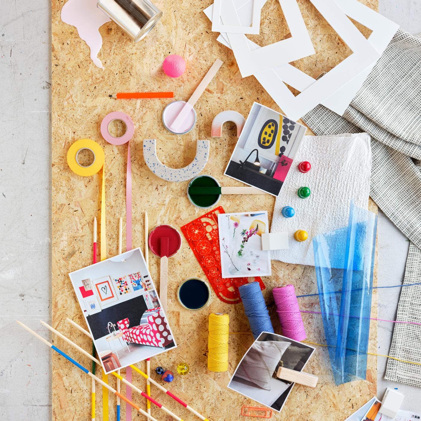A brightly colored mood board with washi tapes, spools of thread, white cardboard frames and photographs.