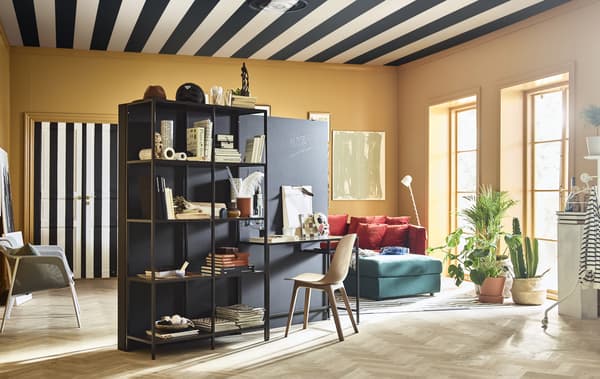 A brightly coloured, creative living room is furnished with a stand-alone wall and work station in the centre of the room.