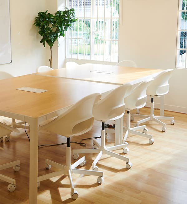 A brightly lit area featuring wooden tables and white chairs. 