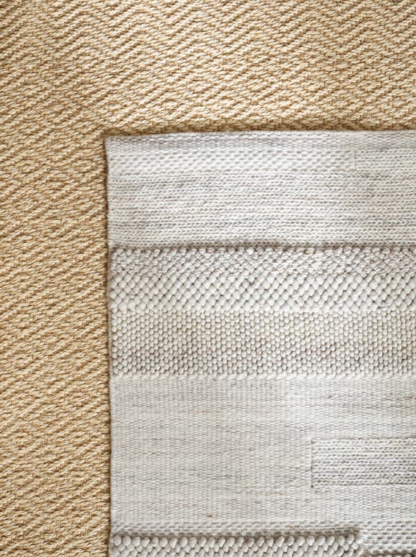 A BRÖNDEN rug lying symmetrically on top of a VISTOFT rug. Both are in light, natural colours with subtle patterns.