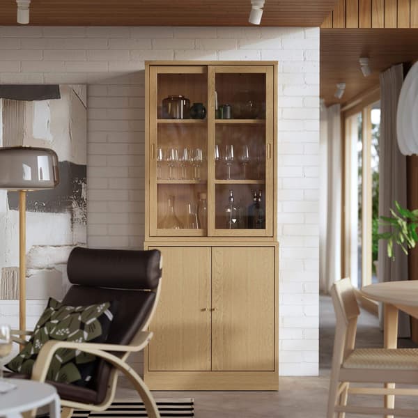 A brown bookcase in a living room with glass inside of it.