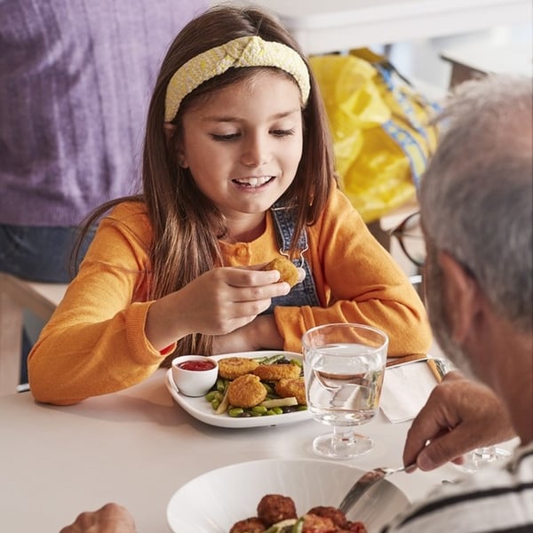 A brown-haired child wearing an orange long-sleeve shirt eats a meal with their grandparent in the Swedish restaurant.