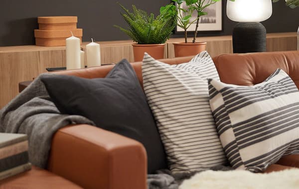 A brown leather sofa with three cushions with various gray and white patterns, and framed pictures on a dark gray wall.