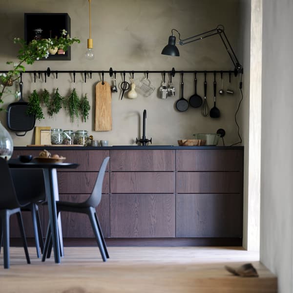 A brown SINARP kitchen with a black table and anthracite chairs, plus black HULTARP rails with kitchen items on hooks.