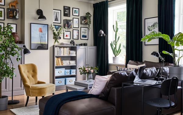A brown sofa in a light colored room with gray storage cabinets and dark colored curtains.