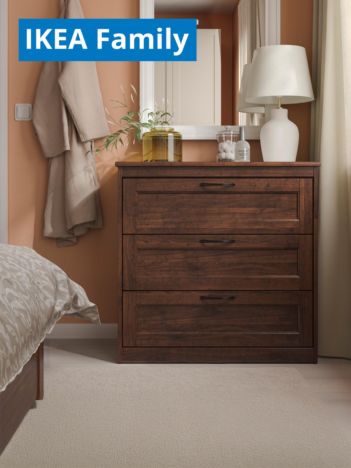A brown SONGESAND chest of 3 drawers at the corner of the bedroom next to the window. On the top left corner, a blue tag with white text that reads "IKEA Family price".