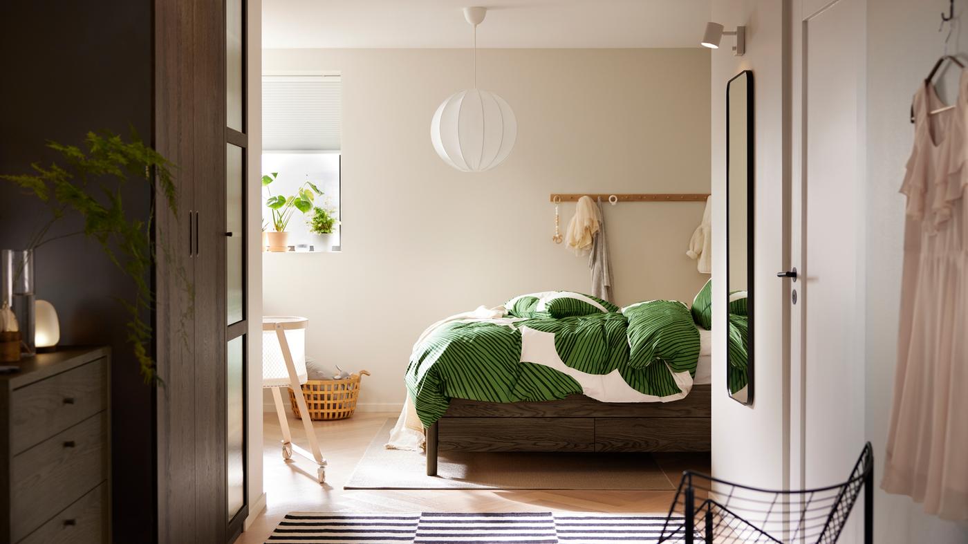 A brown stained oak veneer TONSTAD bed with storage with KUNGSCISSUS bed linen stands under a white REGNSKUR pendant lamp.