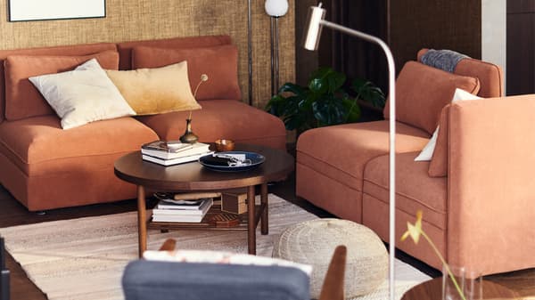 A brown-toned living room containing two VALLENTUNA sofas in rust, a beige rug with a coffee table on it.