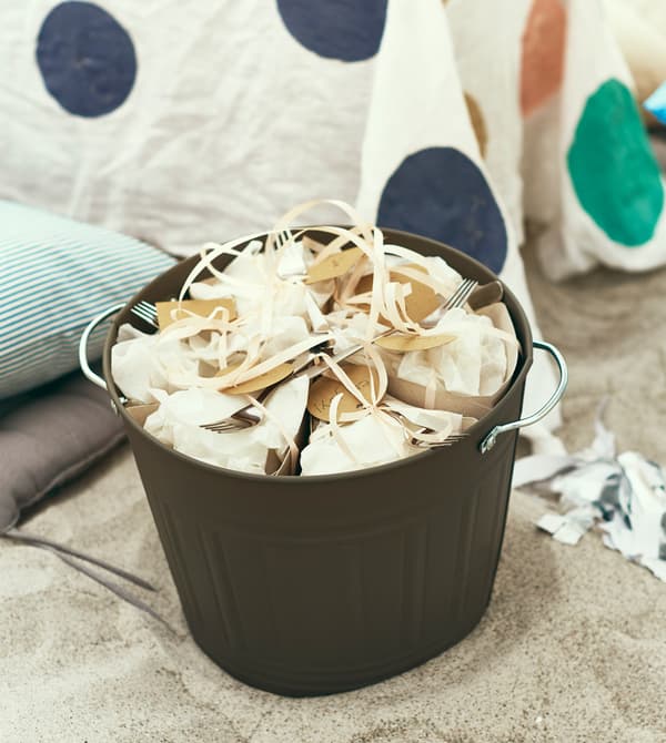 A bucket full of packet-up food sits in the sand.