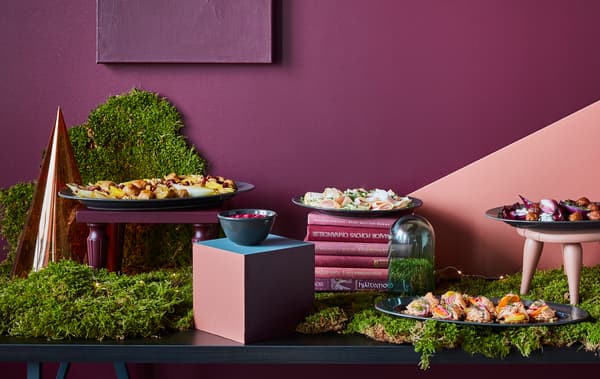 A buffet table is set with food, greenery, and decorations in shades of dark red and green.