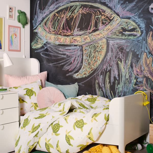 A BUSUNGE bed is dressed in a BLÅVINGAD green turtle duvet cover with cushions in front of a chalkboard wall.