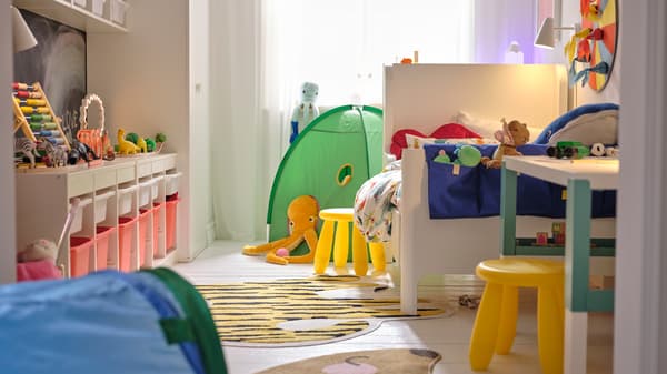 A BUSUNGE extendable bed on one side of a small bedroom with a yellow MAMMUT stool by it and a green play tent behind it.