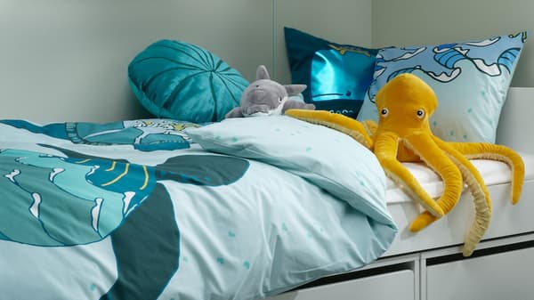 A BUSUNGE white bed is dressed in a BLÅVINGAD green turtle duvet cover with cushions in front of a chalkboard wall.