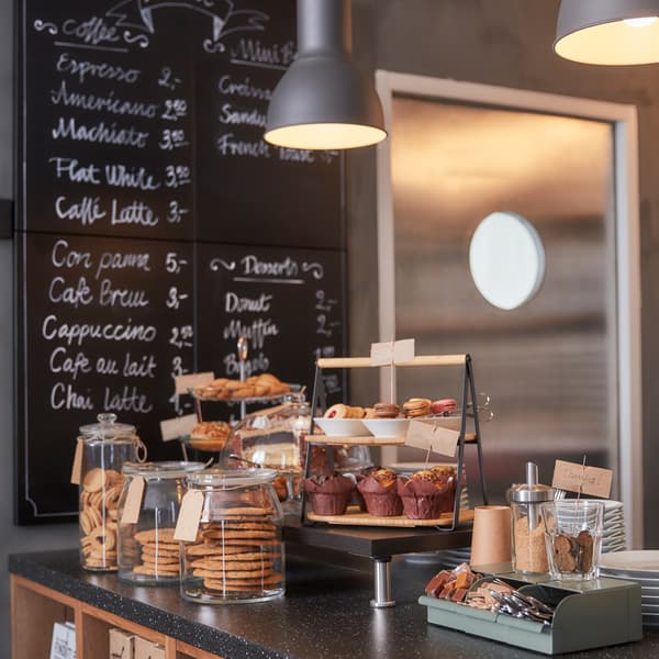 A café kitchen counter with glass jars filled with biscuits, a serving tray in two levels, a green box and white plates.