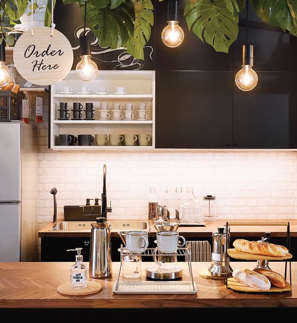 A café ordering area featuring two wooden countertops with coffee-making accessories and plants at the top of the ceiling.