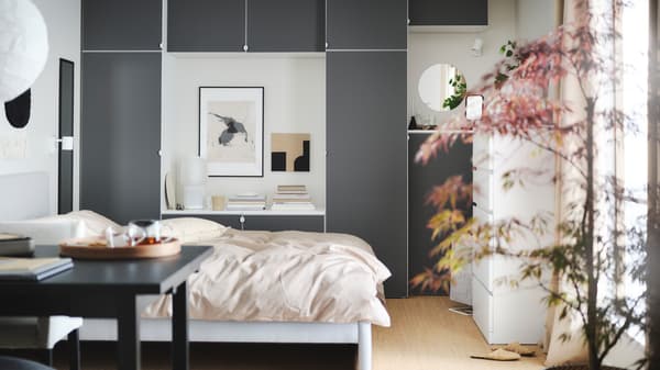 A calm bedroom with a large bed, a wooden desk, a dynamic grey wardrobe and a round lamp hanging from the ceiling.