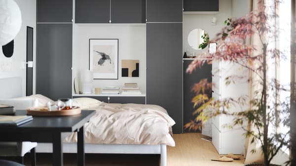 A calm bedroom with a large bed, a wooden desk, a dynamic grey wardrobe and a round lamp hanging from the ceiling.
