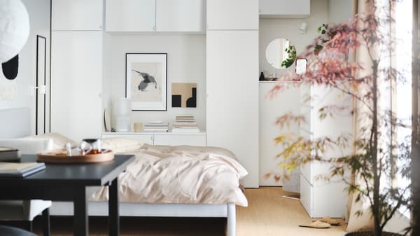 A calm bedroom with a large bed, a wooden desk, a dynamic white wardrobe and round lamps hanging from the ceiling.
