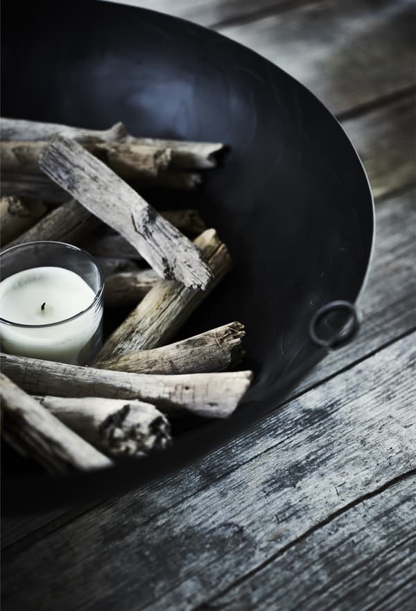 A candle and wood in a black bowl.