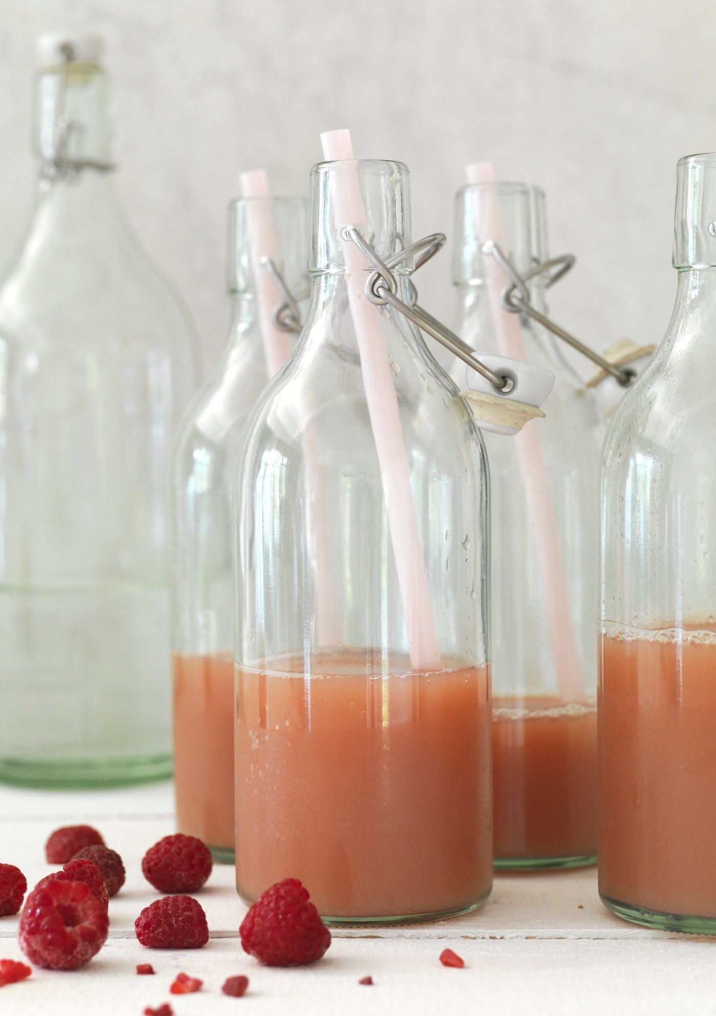 A carafe of a drink with fresh fruit and herbs is next to an open bottle of KORKEN, a refreshing elderflower syrup.