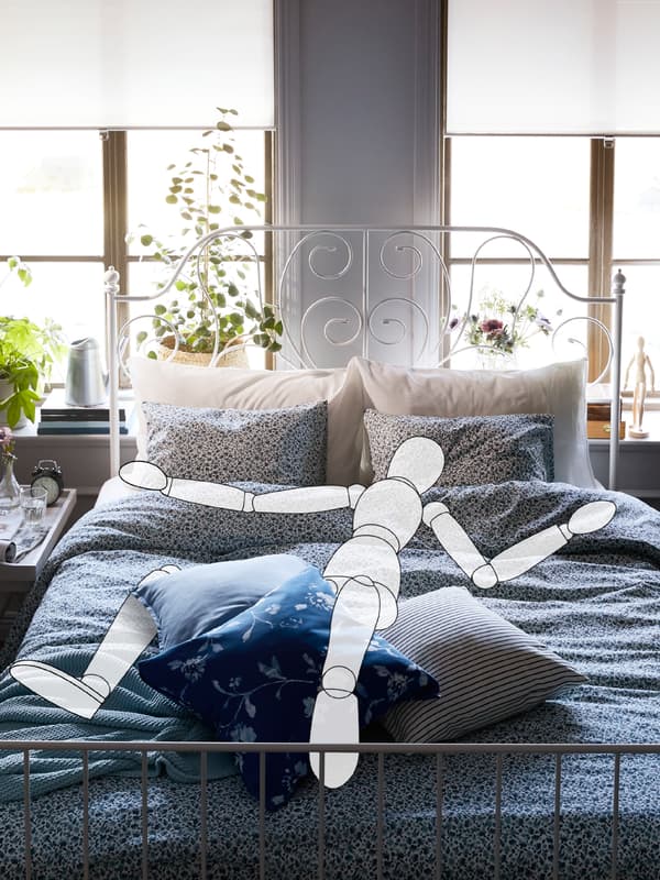 A cartoon drawing of a person sleeping on a LEIRVIK bed with VATTENMYNTA bed linen. Behind the bed are two large windows.