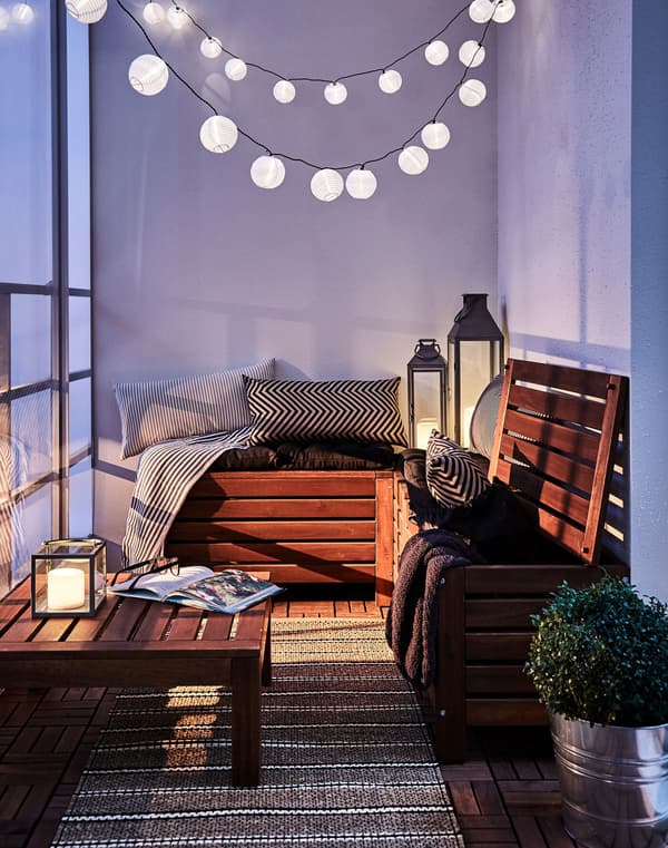 A chain of lights hanging over the corner of a cosy terrace with a comfortable chair and coffee table.