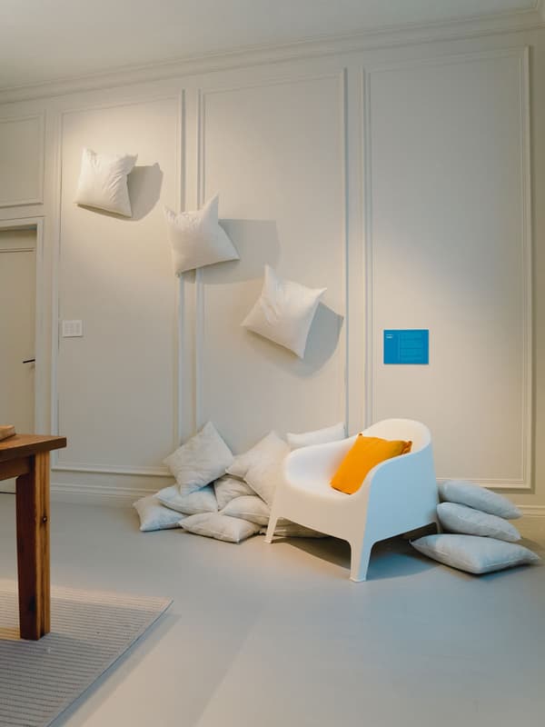 A chair and several pillows are on display. Some pillows are stacked on the floor while others are taped to the wall.
