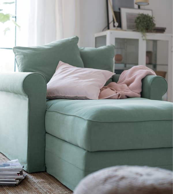 A chaise longue in light green with pink cushions.