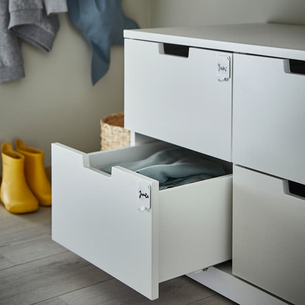 A chest of drawers and one drawer is open. The drawers have PLUTT hooks on them, and names are written here to help organize.