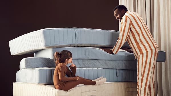 A child and a man are smiling and looking at each other in a stack of mattresses.