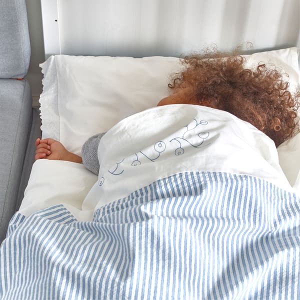 A child asleep in bed, wrapped in an IKEA GULSPARV quilt cover, in a white and blue striped pattern, with embroidered flowers.