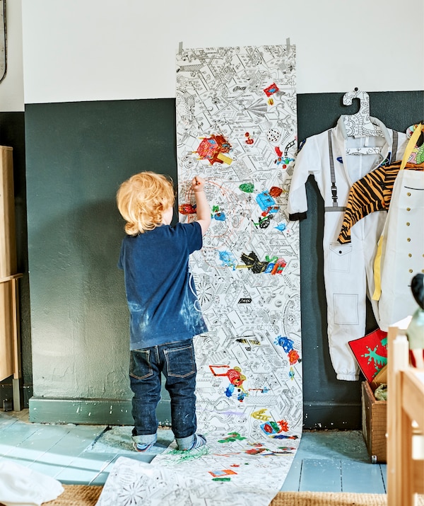 A child coloring in an illustrated roll of paper attached to the wall.