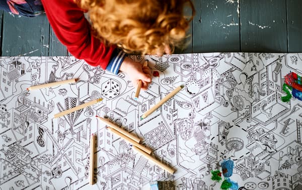 A child coloring in an illustrated sheet of paper on a painted wooden floor.