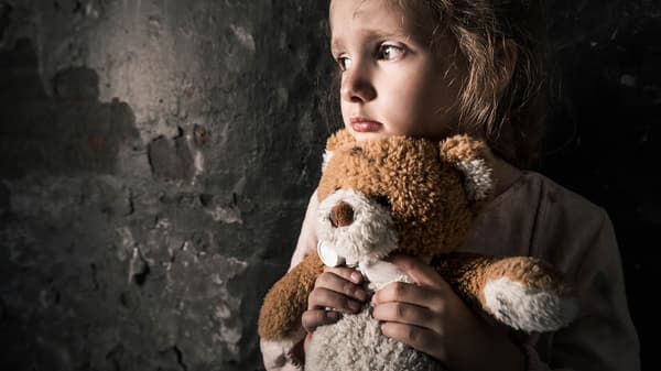a child holding a teddy bear with a sad look on their face