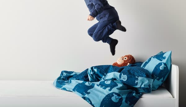 A child in blue pajamas is jumping on the bed.
