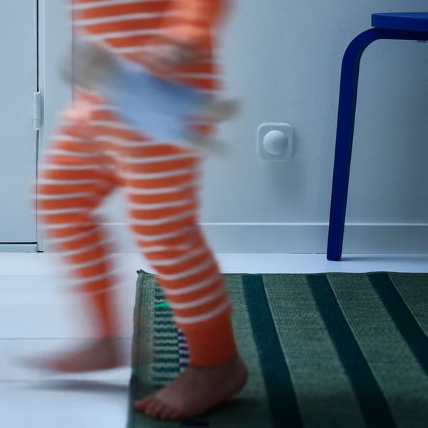 A child in orange striped pyjamas walking across a room, captured in motion blur near a motion sensor.