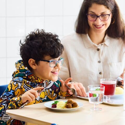 A child is sitting next to his mother, he is eating a dinner at IKEA. They both look happy.