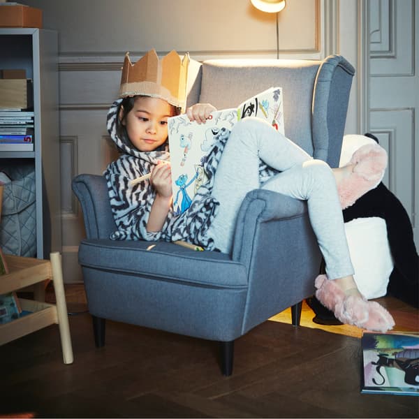 A child lounging in miniature version of a grey IKEA STRANDMON armchair.